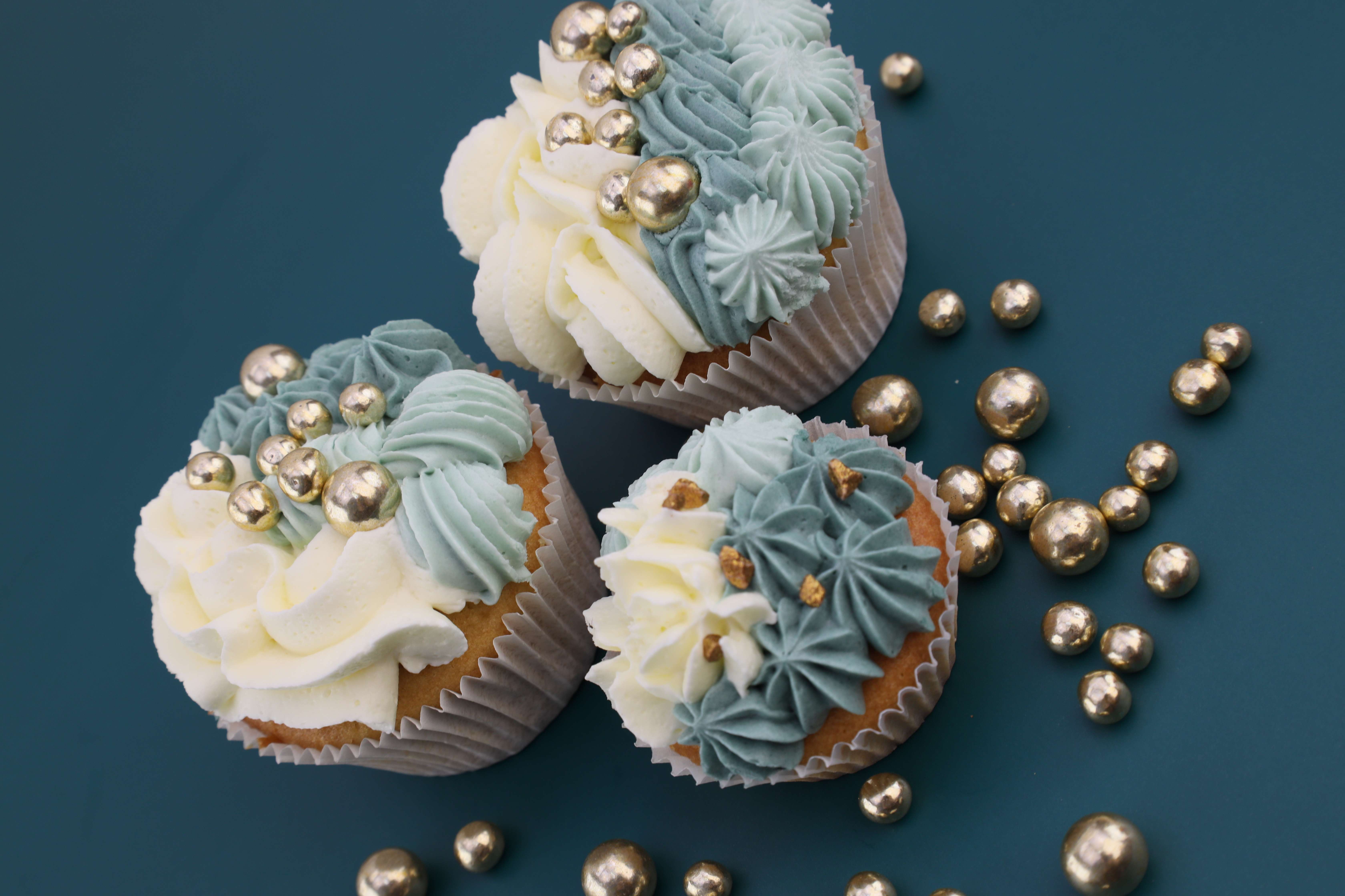 Köstlicher Muffins aus eukalyptusblauer und weißer Buttercreme mit goldenen essbaren Perlen oben drauf. 